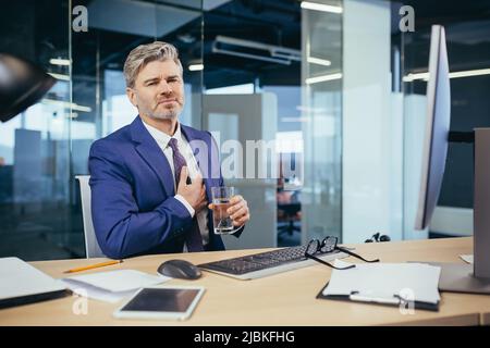 L'uomo d'affari dai capelli grigi ha un dolore toracico severo, un lavoratore esperto che lavora ad una scrivania nell'ufficio Foto Stock