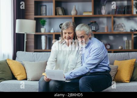 Membro della famiglia di capelli grigi anziani che riceve la lettera o il documento che gioisce seduto a casa. Allegro marito e moglie si ritirees sorridendo mentre si legge il Foto Stock