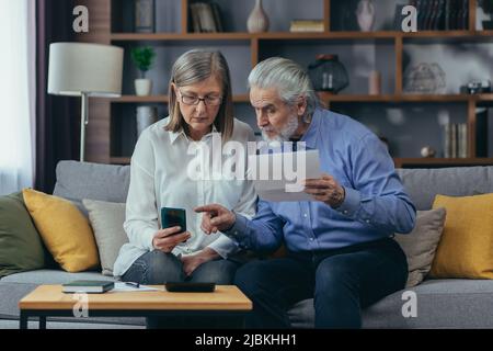 coppia di famiglie anziane, uomo anziano e donna dai capelli grigi pagano i servizi inserire i documenti di dati utilizzando l'applicazione smartphone mobile. Ritiri a casa Foto Stock