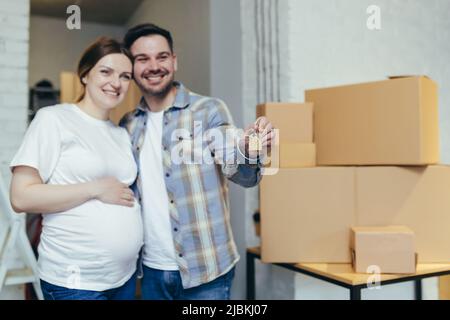 Giovane e felice famiglia che aspetta un bambino. Donna incinta e marito si trasferirono in una nuova casa, appartamento. Disimballare le scatole con le cose. Abbracciante, sorridente Foto Stock