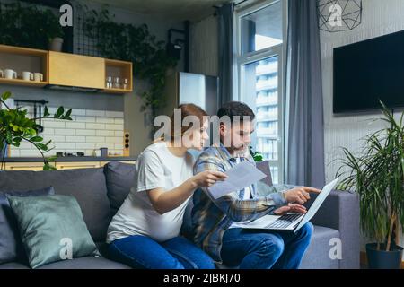 Coppia sposata, marito e donna incinta che lavorano su laptop, documenti a casa Foto Stock