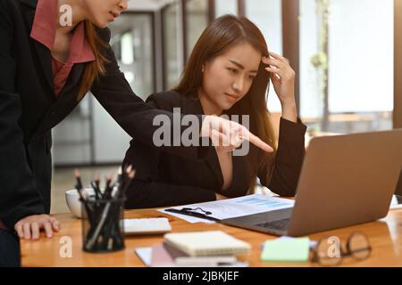 Una giovane dipendente asiatica sollecitata riceve un cattivo feedback sul suo progetto di lavoro e sulle sue prestazioni dal suo manager. Foto Stock