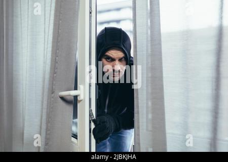 ladro maschile in abiti neri cercando di rompere la serratura porta in casa Foto Stock