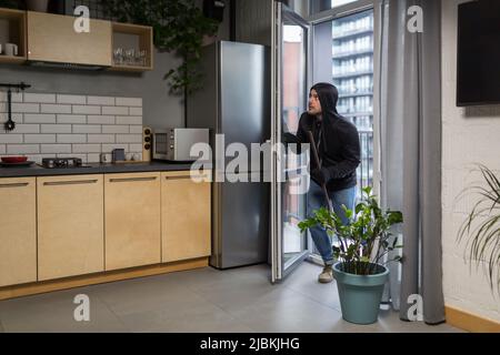 ladro maschile in abiti neri cercando di rompere la serratura porta in casa Foto Stock