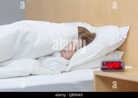 Foto ravvicinata di una donna insonne e turbata che si trova a letto sotto una coperta, cercando di addormentarsi Foto Stock