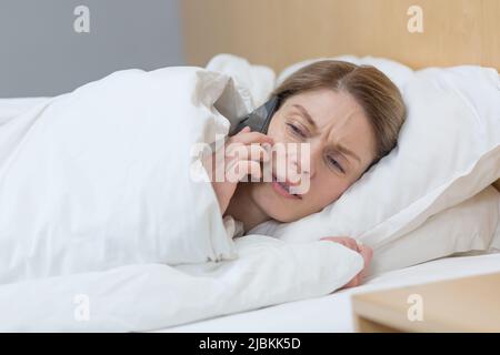 Primo piano, foto di una donna di mezza età a casa, sdraiata a letto, triste e depresso parlare al telefono Foto Stock