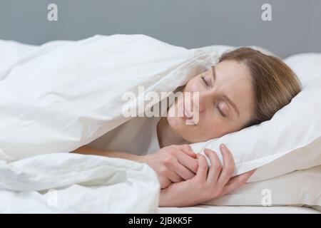 Primo piano di una donna che dorme sotto una coperta sorridendo in un sogno Foto Stock