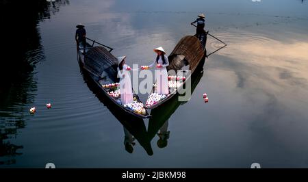 Città di Hue, Vietnam - 28 aprile 2022: Due ragazze vietnamite con il tradizionale ao dai bianco stanno accendendo le candele per pregare nel fiume. Ao dai è un famoso t Foto Stock