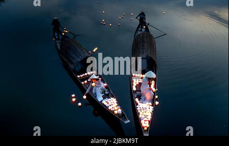 Città di Hue, Vietnam - 28 aprile 2022: Due ragazze vietnamite con il tradizionale ao dai bianco stanno accendendo le candele per pregare nel fiume. Ao dai è un famoso t Foto Stock