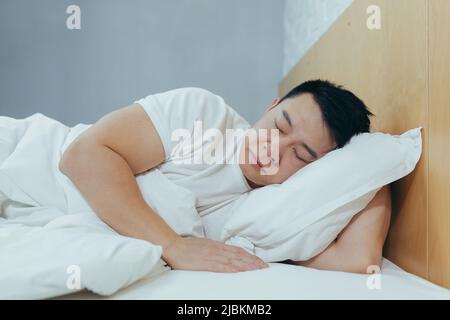 Triste asiatico giaceva in un letto sotto una coperta, un uomo depresso al mattino Foto Stock