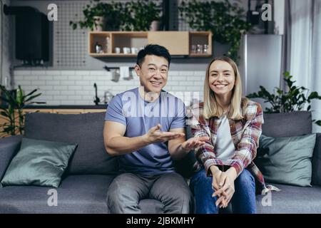 Videochiamata di coppia felice, donna introduce amici a marito, famiglia felice a casa sul divano Foto Stock