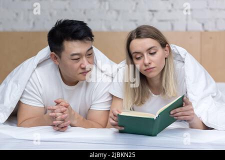 Felice coppia asiatica in amore e donna che si trova insieme a letto e la lettura di un libro Foto Stock
