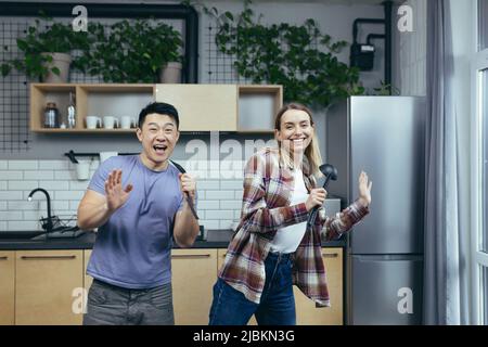 Felice giovane asiatico uomo e donna coppia cantare e ballare insieme in cucina, divertirsi insieme, la famiglia innamorata Foto Stock