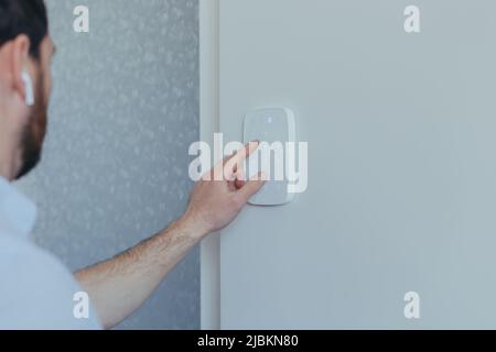 Businessman inserisce il codice di blocco della password sul pannello di allarme, sulla parete bianca, vista posteriore dell'uomo con barba Foto Stock