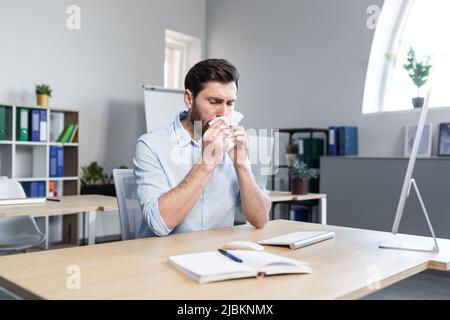 Uomo d'affari malato nell'uomo d'ufficio con allergie starnuti, seduto ad un tavolo con un computer Foto Stock