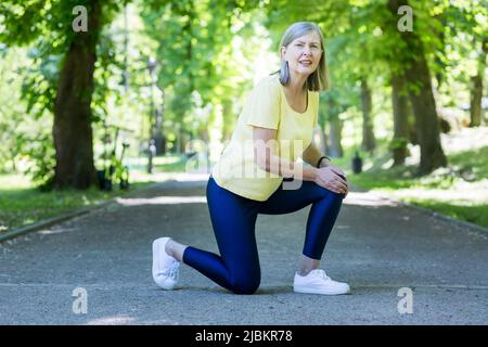 Trauma. Donna bella senior ferito il ginocchio. Tenendo le mani sulla gamba, si sedette. Entra per lo sport e corre nel parco. Foto Stock