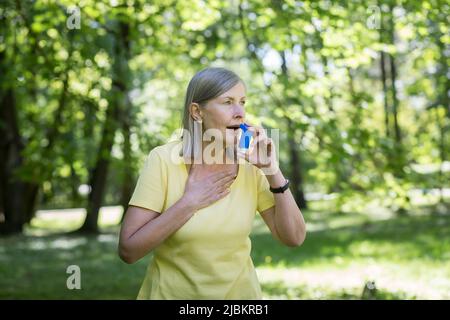 Donna anziana in pensione con asma che respira in un inalatore in un parco estivo Foto Stock