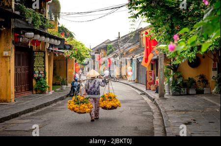 Città antica di Hoi An, provincia di Quang Nam, Vietnam - 1 maggio 2022: Foto di una donna che vende fiori su un paio di cornici di bambù nella città antica di Hoi An, VN Foto Stock