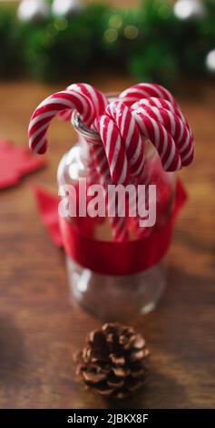 Primo piano verticale di caramelle in un vaso circondato da decorazioni natalizie su un tavolo di legno Foto Stock
