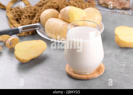 Latte di patate vegano in un bicchiere e tuberi di patate su sfondo grigio tavola di pietra. Latte alternativo a base vegetale e senza lattosio, trendy sano Foto Stock