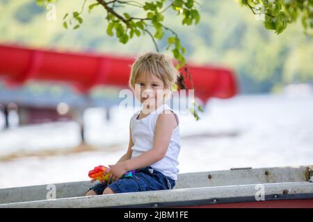 Bambino piccolo, ragazzo biondo, giocando con pop it antistress giocattolo nel parco in una barca in lago Foto Stock