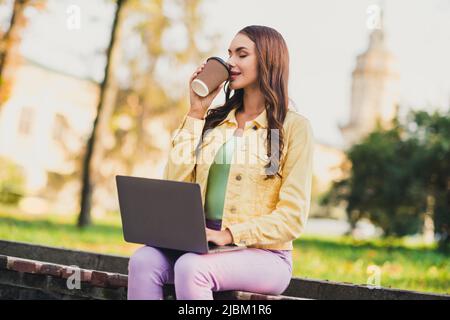 Ritratto di bella ragazza sognante di tendenza copywriter seduta su panca bere latte utilizzando il portatile che viaggia all'estero Foto Stock