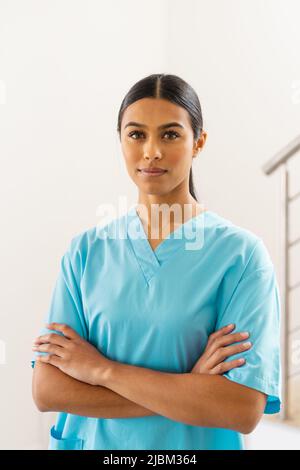 Ritratto di fidato medico biracale giovane femmina con le braccia incrociate in clinica Foto Stock