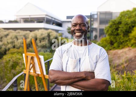 Ritratto di sorridente anziano afro-americano con braccia incrociate in piedi da tela e cavallino Foto Stock