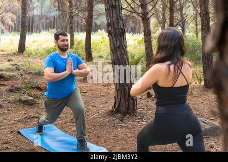 I giovani che praticano lo yoga in una foresta con il loro tappetino blu in una giornata di sole per rilassarsi. Foto Stock