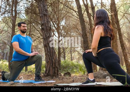 I giovani amici si stendono sui loro tappetini yoga al tramonto in una foresta circondata da alberi. Foto Stock