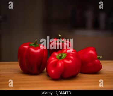 Primo piano di peperoni rossi posti su un tagliere in cucina. Noto anche come peperone dolce, peperone o capsicum. Foto Stock