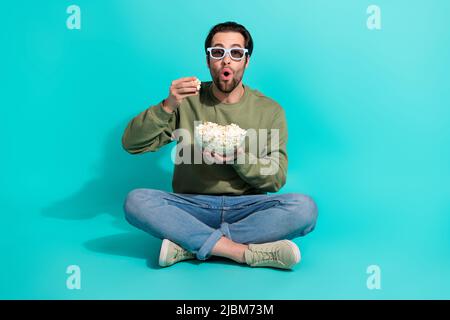 Foto a corpo intero di giovane ragazzo impressionato guardare cinema horror seduta pavimento isolato su sfondo di colore turchese Foto Stock