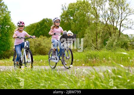 Le sorelle gemelle sono viste guidare le loro biciclette nella campagna. Hanno un volto sorridente felice su di loro mentre si godono il loro giro in bicicletta all'aperto. Foto Stock