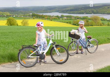 Le sorelle gemelle sono viste guidare le loro biciclette nella campagna. Hanno un volto sorridente felice su di loro mentre si godono il loro giro in bicicletta all'aperto. Foto Stock