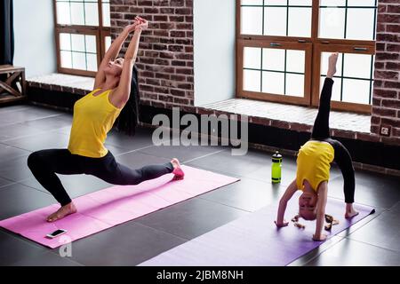 Giovane donna e bambina che fa esercizi di stretching ginnico sul tappeto in palestra. Foto Stock