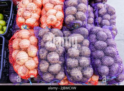 Cipolle e patate fresche e biologiche confezionate in sacchi in vendita sul mercato Foto Stock
