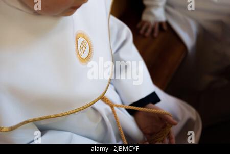 IHS simbolo cristiano su un bambino di comunione. IHS Christogram ricamato con filo d'oro su un'erba bianca. Primo vestito della Santa comunione. Foto Stock
