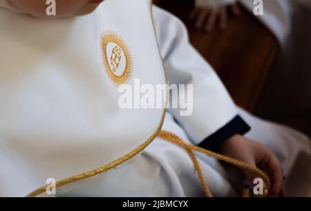 IHS simbolo cristiano su un bambino di comunione. IHS Christogram ricamato con filo d'oro su un'erba bianca. Primo vestito della Santa comunione. Foto Stock