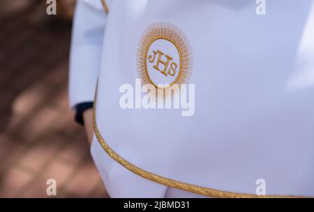 IHS simbolo cristiano su un bambino di comunione. IHS Christogram ricamato con filo d'oro su un'erba bianca. Primo vestito della Santa comunione. Foto Stock