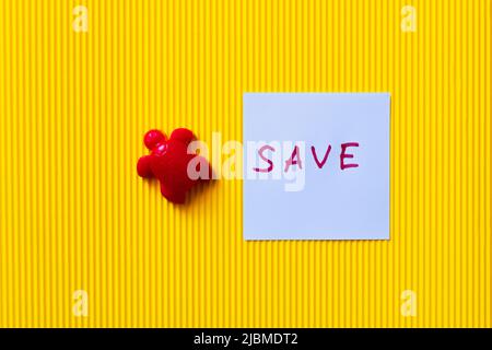 vista dall'alto della tartaruga rossa giocattolo vicino alla carta con caratteri di salvataggio su sfondo giallo testurizzato Foto Stock