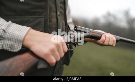 Primo piano di cacciatore uomo carica la cartuccia su fucile pistola in foresta. Foto Stock