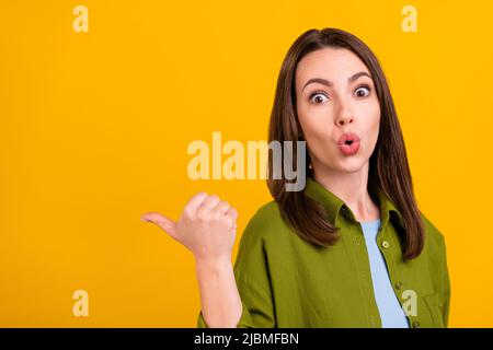 Foto di dolce scioccata giovane donna vestita camicia verde sorridente puntando indietro dito vuoto spazio isolato colore giallo sfondo Foto Stock