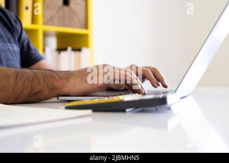 Utilizzando il computer portatile e la calcolatrice, è possibile visualizzare un'immagine ravvicinata delle mani utilizzando il computer portatile e la calcolatrice. Uomo d'affari lavora su un progetto, digitando su tastiera notebook. Foto Stock