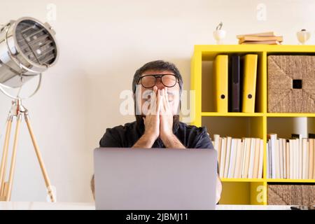 Uomo d'affari stanco, giovane uomo d'affari stanco che gli sfrega gli occhi. Giovane lavoratore confuso, frustrato, triste o depresso. Vista frontale del giovane uomo che usa un computer portatile. Foto Stock