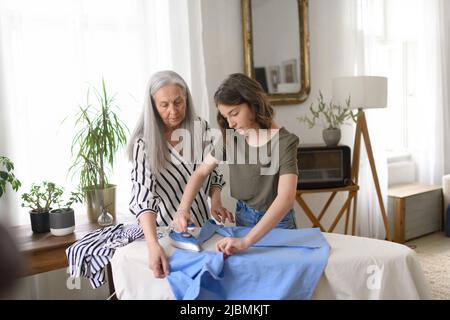 Ragazza adolescente stirare e aiutare con la famiglia chores sua nonna anziana a casa Foto Stock