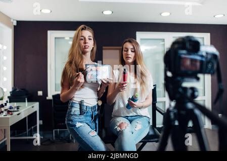 Giovani donne che tengono prodotti di bellezza fare un video su cosmetici per videoblog Foto Stock