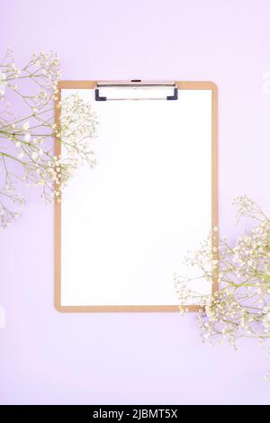 Desktop viola con clipboard e fiori di gypsofila. Disposizione piatta, vista dall'alto, mockup. Foto Stock
