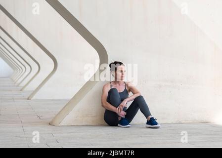 Adatta donna seduta con la schiena a un muro di cemento, rilassarsi dopo l'esercizio all'esterno. Foto Stock