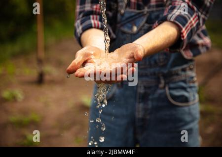 Primo piano mani e acqua maschile, contadino lavano le braccia con acqua cristallina in giardino al mattino. Concetto di lavoro, occupazioni, prodotti biologici, ecologia Foto Stock