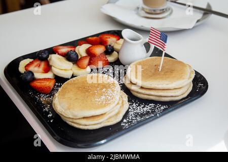 Frittelle e frutta e panna servite su un vassoio rettangolare con una bandiera americana in miniatura inserita nelle frittelle. Foto Stock